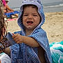 Eden a rejoint le concours — aidez-le/la à gagner de superbes lots ! toddler, child, beach, towel, hooded_towel, striped_clothing, smiling, sand, ocean, water, summer, vacation, playful, person, outdoor, sunny, holiday, happy, baby, cute