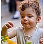 child, toddler, curly_hair, flower, yellow_flower, nature, outdoor, daylight, cute, portrait, baby, exploring, greenery, garden, casual_clothing, sleeveless_shirt, skin, face, hand, focus