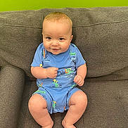 Roman is registered to the contest to win money with this photo: baby, child, smile, blue_onesie, couch, green_wall, sitting, barefoot, cute, infant, face, happy, plush, person, indoor, cozy, skin, legs, hand, expression