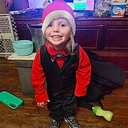 Joseph is registered to the contest to win money with this photo: child, toddler, smiling, santa_hat, red_shirt, black_vest, bowtie, shoes, wooden_floor, television, streaming_services, bowl, sippy_cup, jacket, indoor, happy, person, home, clothing, furniture