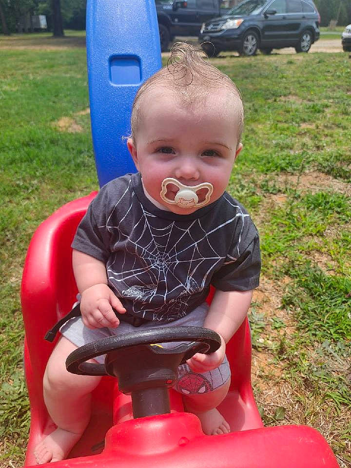 Colson is registered to the contest to win money with this photo: automotive_exterior, baby, baby_toddler_clothing, child, family_car, fun, grass, lap, leisure, motor_vehicle, person, photograph, plant, play, recreation, sitting, summer, tire, toddler, tree