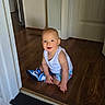toddler, child, indoor, smiling, white_tank_top, shorts, blue_sneaker, barefoot, wooden_floor, doorway, home_interior, happy, sitting, cute, young_child, person, floor, light, casual_clothing, portrait