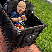 Sage joined the competition — help win amazing prizes! baby, child, wagon, toy, grass, brick_pavement, outdoor, smiling, happy, seat, clothing, blue_shirt, red_shorts, sunny, daytime, person, playtime, cute, infant, stroller