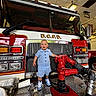 Sage joined the competition — help win amazing prizes! toddler, child, fire_truck, firehose, red, blue_clothing, indoor, vehicle, hose, metal_surface, smiling, person, shiny, equipment, industrial, small_child, cute, standing, casual_clothing, emergency_vehicle