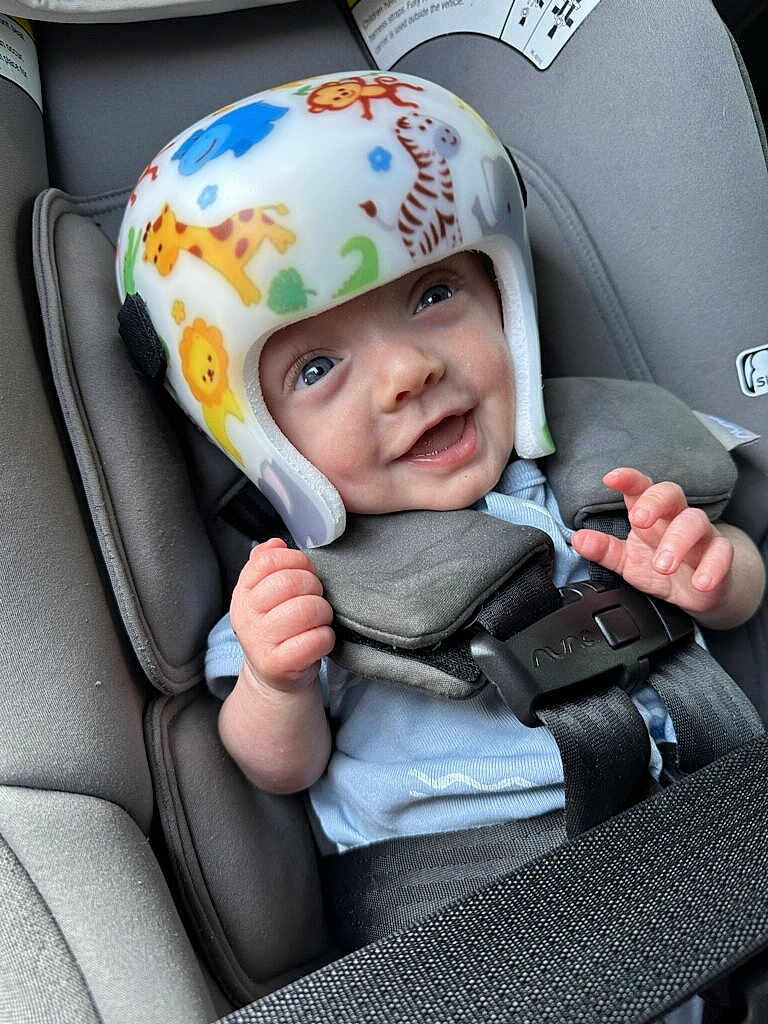 Felix is registered to the contest to win money with this photo: baby, helmet, car_seat, smile, blue_eyes, animal_print, infant, child, safety, seatbelt, cute, happy, clothing, hand, headgear, closeup, transportation, car_interior, protection, infancy