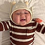baby, infant, child, hat, pom_poms, striped_clothing, brown_and_white, smiling, happy, cute, cheeks, lying_down, blanket, soft, warm, clothing, portrait, one_person, indoor, baby_garment