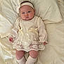 baby, infant, child, bed, blanket, headband, bow, cream_color, lace, socks, cute, expression, lying_down, soft_texture, clothing, portrait, indoors, skin, hands, legs
