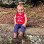 toddler, child, smiling, sitting, red_shirt, boots, rock, nature, outdoor, curly_hair, greenery, leaves, forest_floor, tank_top, happy, young_child, playful, casual_clothing, daylight, portrait