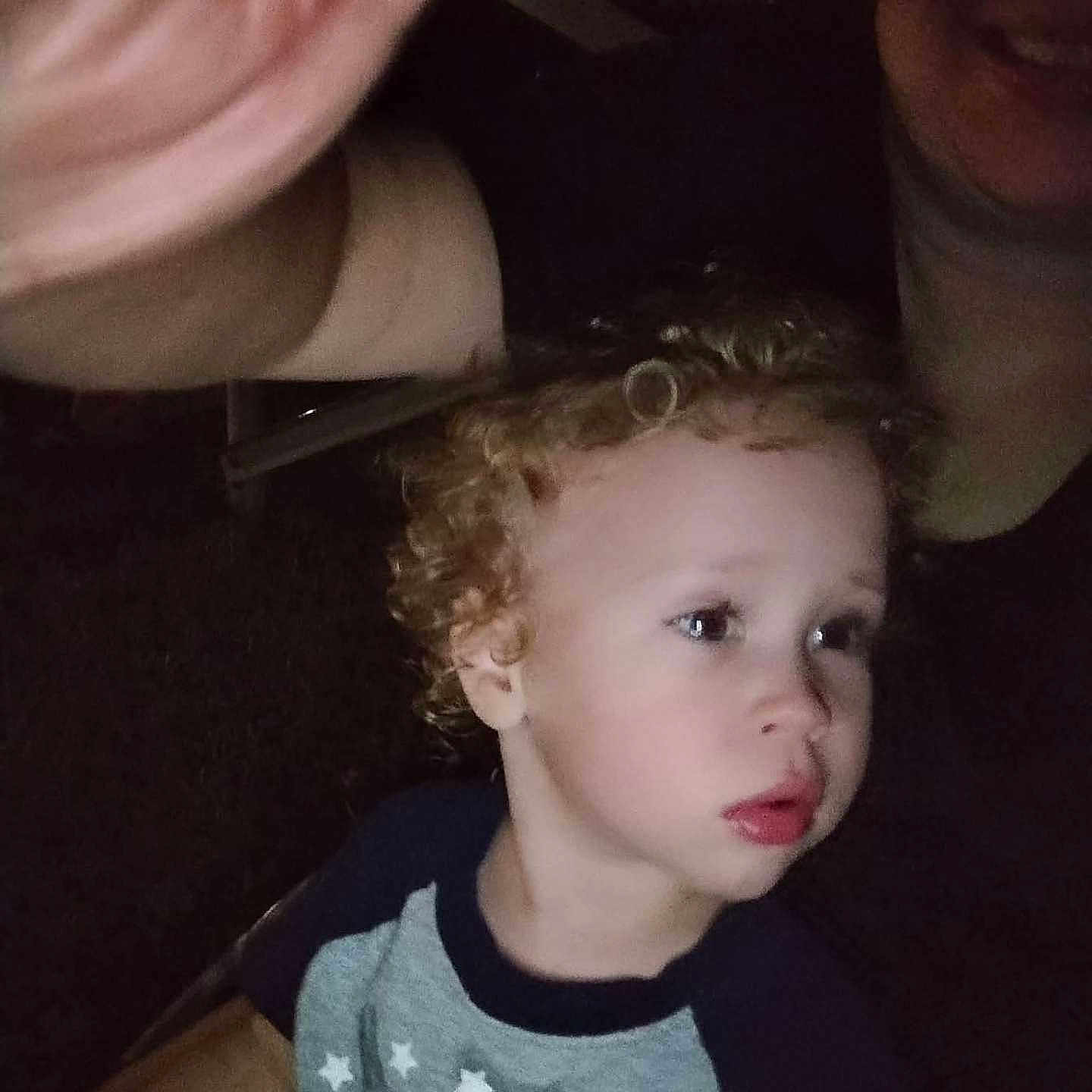 Bryce is registered to the contest to win money with this photo: child, curly_hair, person, adult, hand, night, dark, shirt, toddler, face, portrait, expression, looking_away, indoor, casual_clothing, blurry, selfie, closeup, skin, head