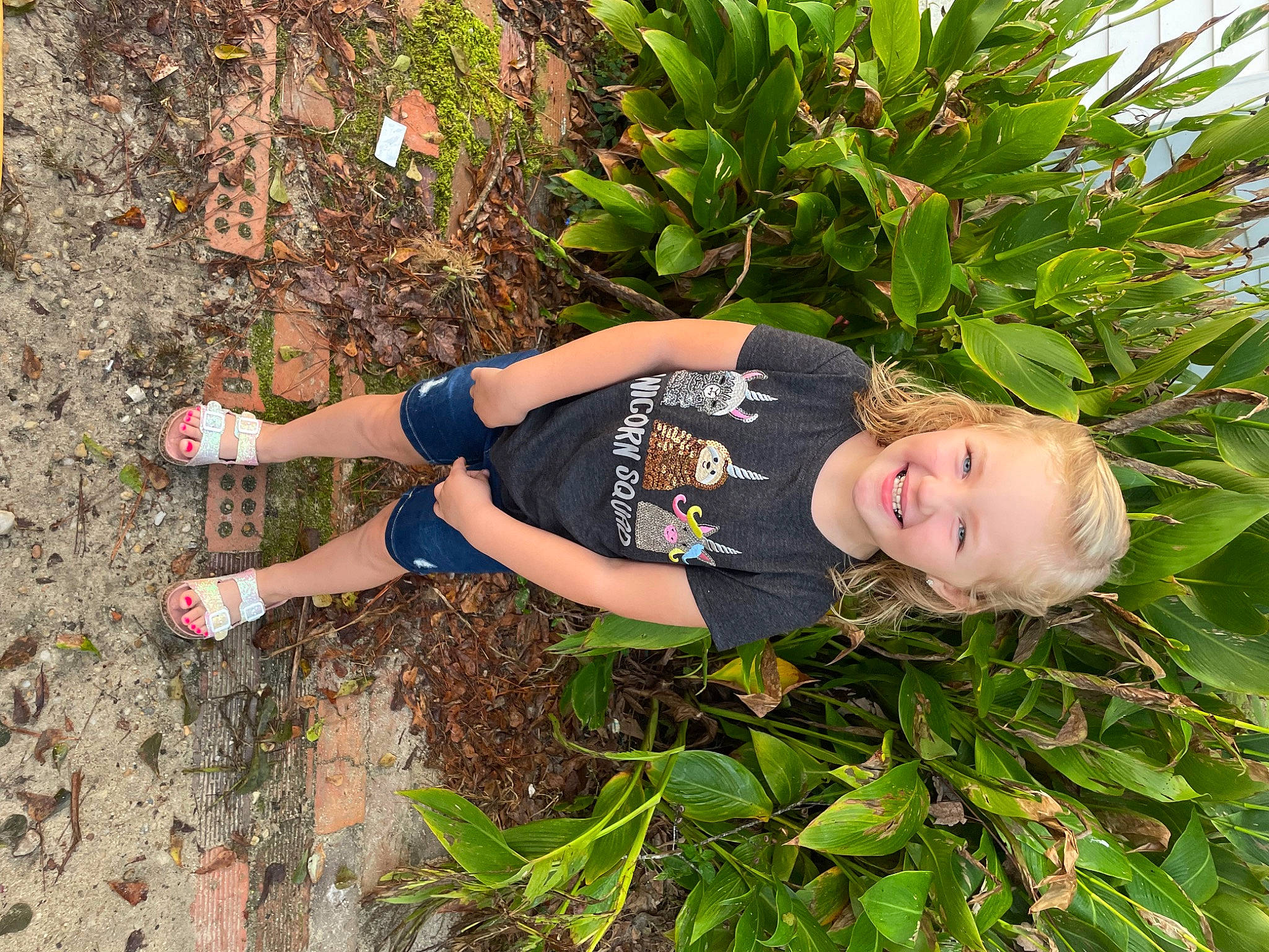 Anslee is registered to the contest to win money with this photo: child, flowering_plant, garden, grass, grass_family, groundcover, happy, human_leg, joy, knee, leisure, people_in_nature, person, plant, shorts, shrub, smile, soil, t_shirt, terrestrial_plant