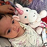 baby, child, infant, plush_toy, unicorn, soft_toy, bed, blanket, hand, cute, portrait, indoor, clothing, floral_pattern, sleepwear, comfort, relaxation, closeup, face, young_child