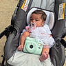 baby, stroller, pacifier, camera, white_clothing, outdoor, child, infant, cute, seat, foot, head, toy, transport, person, baby_clothes, baby_accessory, baby_bottle_holder, infant_seat, baby_girl