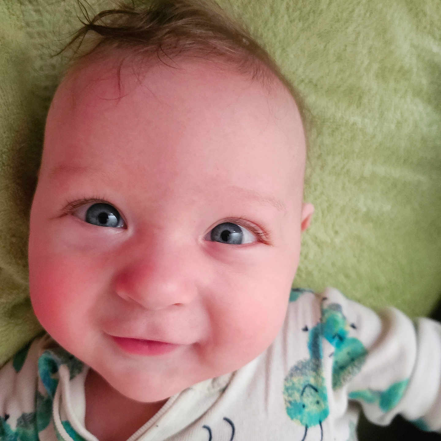 Jimmy is registered to the contest to win money with this photo: baby, infant, smiling, face, blue_eyes, onesie, caterpillar_print, hair, blanket, close_up, cute, child, happy, portrait, skin, lying_down, expression, soft_texture, indoors, person