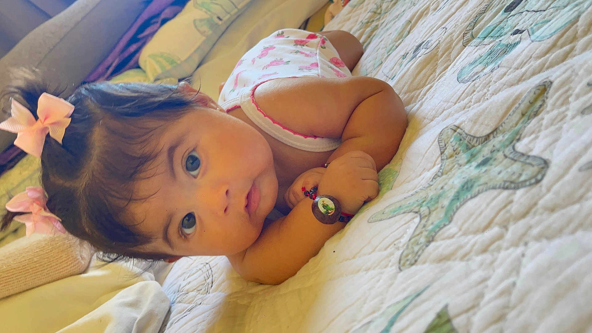 Leilani is registered to the contest to win money with this photo: baby, child, infant, bow, bracelet, quilt, starfish, bed, face, eyes, hair, pink, clothing, lying_down, portrait, cute, skin, hand, indoor, person