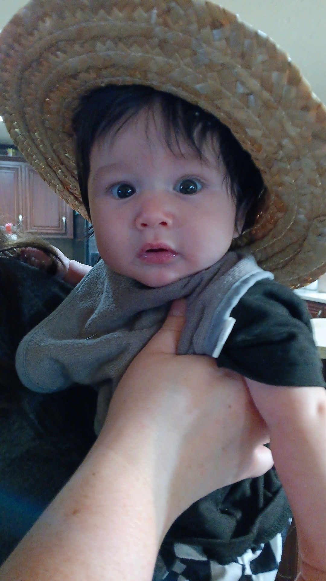 Enzo joined the competition — help win amazing prizes! baby, child, hat, straw_hat, face, hand, indoor, kitchen, curious, person, clothing, holding, adult_hand, black_hair, wide_eyes, expression, infant, portrait, cute, young