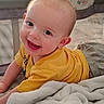 baby, baby_bed, bed, blanket, child, close_up, clothing, cozy, eyes, face, happy, indoor, infant, joyful, laughing, photography, portrait, sitting, smiling, yellow_shirt