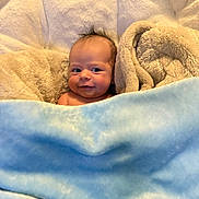 Khoyn is registered to the contest to win money with this photo: baby, blanket, blue_blanket, beige_blanket, smile, face, infant, cozy, soft_texture, child, cute, hair, expression, wrapped, comfort, portrait, indoors, warmth, skin, nest