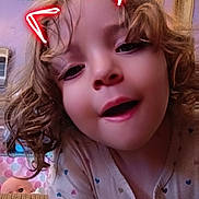 Ronni is registered to the contest to win money with this photo: child, curly_hair, face, indoor, neon_ears, playful, portrait, pajamas, person, cozy, home, doll, bedroom, curtains, window, smiling, cute, expression, closeup, casual