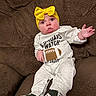 baby, infant, child, portrait, sitting, couch, brown_couch, yellow_bow, headband, white_outfit, football_outfit, sneakers, raised_hand, waving, wide_eyes, smiling, indoor, close_up, fashion, photography