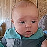 Montie is registered to the contest to win money with this photo: arm, baby, blue_clothing, camera, child, close_up, face, furniture, head, home, indoor, infant, looking_at_camera, person, portrait, safe, sitting, turquoise_shirt, wide_eyed, wooden_wall