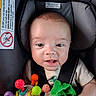 baby, infant, child, car_seat, portrait, face, smiling, awake, indoor, vehicle, safety_harness, colorful_toys, toy, blanket, green_blanket, seated, close_up, brown_hair, casual_clothing, photography