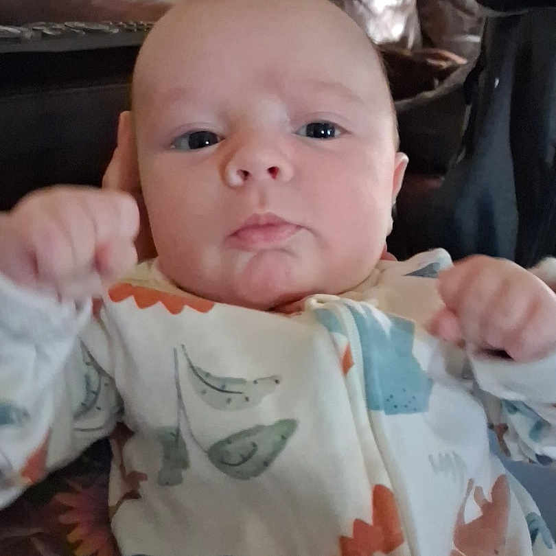 Montie joined the competition — help win amazing prizes! baby, blue_eyes, child, clothing, couch, cozy, cute, dinosaur_pattern, expression, face, fist, hand, indoor, infant, leather, newborn, onesie, person, portrait, soft_lighting
