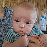 Montie is registered to the contest to win money with this photo: adult_hands, baby, bottle, candid, caregiver, child, closeup, clothing, eyes, face, family, held, indoor, infant, photography, portrait, sitting, striped_shirt, wide_eyed, wooden_background