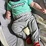 baby, child, infant, hat, blue_eyes, green_shirt, reebok_logo, gray_pants, red_socks, baby_seat, cushion, smiling, indoors, carpet, clothing, person, cute, relaxed, portrait, young