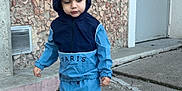 Naïm a rejoint le concours — aidez-le/la à gagner de superbes lots ! toddler, child, hoodie, tracksuit, blue_clothing, sneakers, concrete, pavement, stone_wall, urban, door, outdoor, standing, casual, young_child, person, daylight, sidewalk, fashion, hood