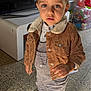 Naïm participe au concours pour gagner de l'argent avec cette photo : child, toddler, indoor, jacket, overalls, brown_jacket, shoes, floor, tiles, toy_box, toys, face, person, standing, curious, clothing, casual, light, shadow, portrait