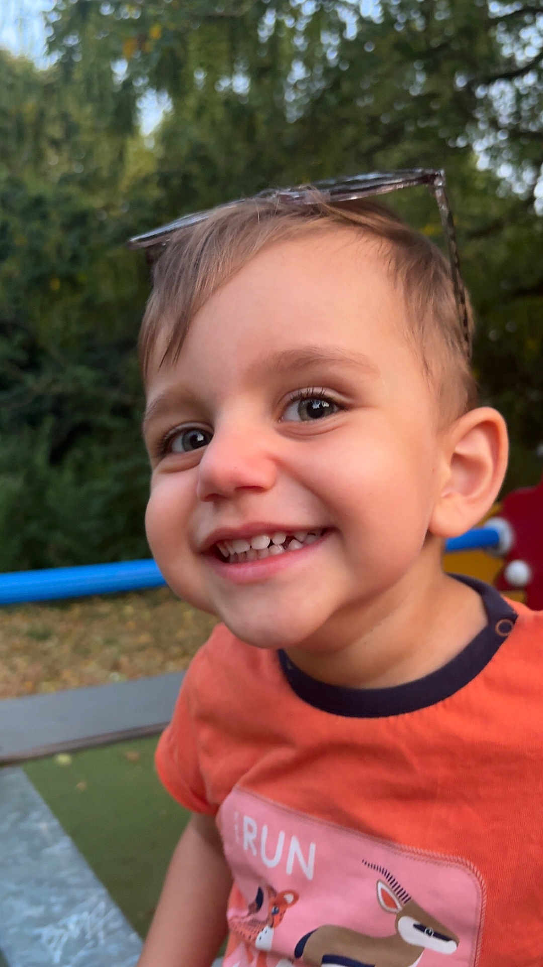 Naïm participe au concours pour gagner de l'argent avec cette photo : child, toddler, smiling, face, outdoor, playground, sunglasses, happy, short_hair, person, shirt, animal_graphic, nature, greenery, daylight, closeup, cute, fun, cheerful, casual_clothing