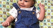 Cylan is registered to the contest to win money with this photo: baby, carpet, casual_clothing, child, cushion, cute, denim_overalls, face, floor, happy, head, indoor, infant, lying_down, patterned_cushion, portrait, raised_arm, small_child, smiling, white_shirt