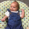 Cylan is registered to the contest to win money with this photo: baby, denim_overalls, smiling, lying_down, cushion, patterned_cushion, infant, cute, happy, raised_arm, white_shirt, carpet, floor, small_child, indoor, portrait, casual_clothing, face, head, child