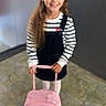 child, girl, smiling, long_hair, striped_shirt, black_dress, pink_suitcase, disney_princesses, indoor, floor, concrete_floor, backpack, happy, standing, school, young, portrait, casual_clothing, first_day, kindergarten