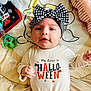 baby, infant, headband, bow, shirt, text, halloween, toy, blanket, lying_down, cute, face, clothing, child, indoors, smiling, person, expression, playful, colorful