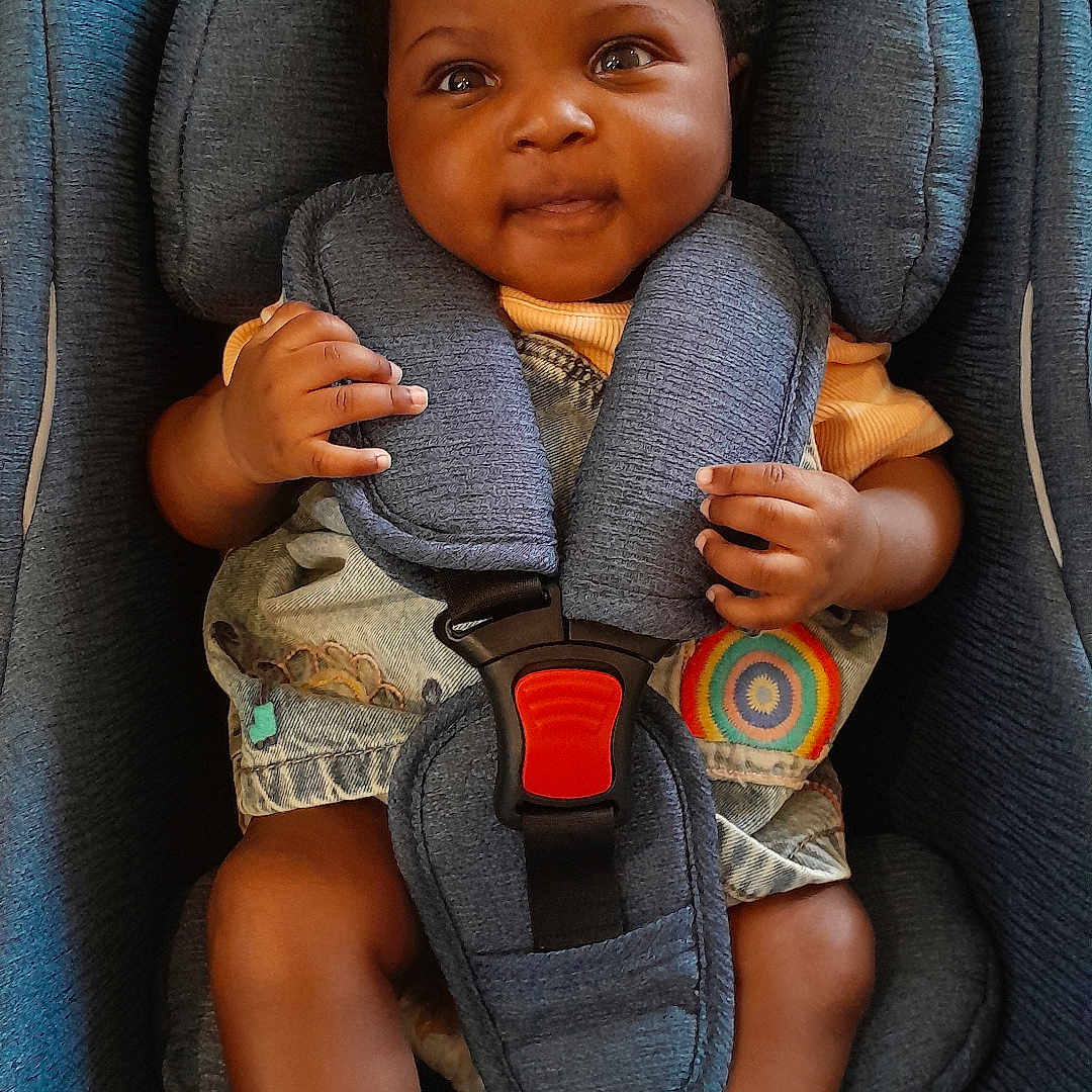 Precious is registered to the contest to win money with this photo: baby, blue, car_seat, child, clothing, colorful, cute, denim, face, hands, happy, indoor, infant, legs, pattern, seatbelt, sitting, smiling, socks, young