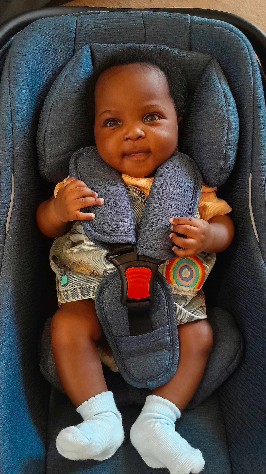 Precious is registered to the contest to win money with this photo: baby, child, car_seat, seatbelt, blue, socks, clothing, infant, face, hands, legs, cute, smiling, indoor, sitting, colorful, pattern, denim, happy, young