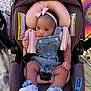 baby, baby_accessory, car_safety, car_seat, child, child_seat, clothing, colorful_background, comfort, cute, denim_overalls, floral_shoes, footwear, headband, indoors, infant, person, pink_bow, sitting, small_child