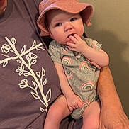 Tilly-May is registered to the contest to win money with this photo: adult, baby, child, closeup, clothing, curious_expression, fingers, floral_design, glasses, hand, hat, indoor, infant, lap, onesie, person, purple_shirt, sitting, skin, wall