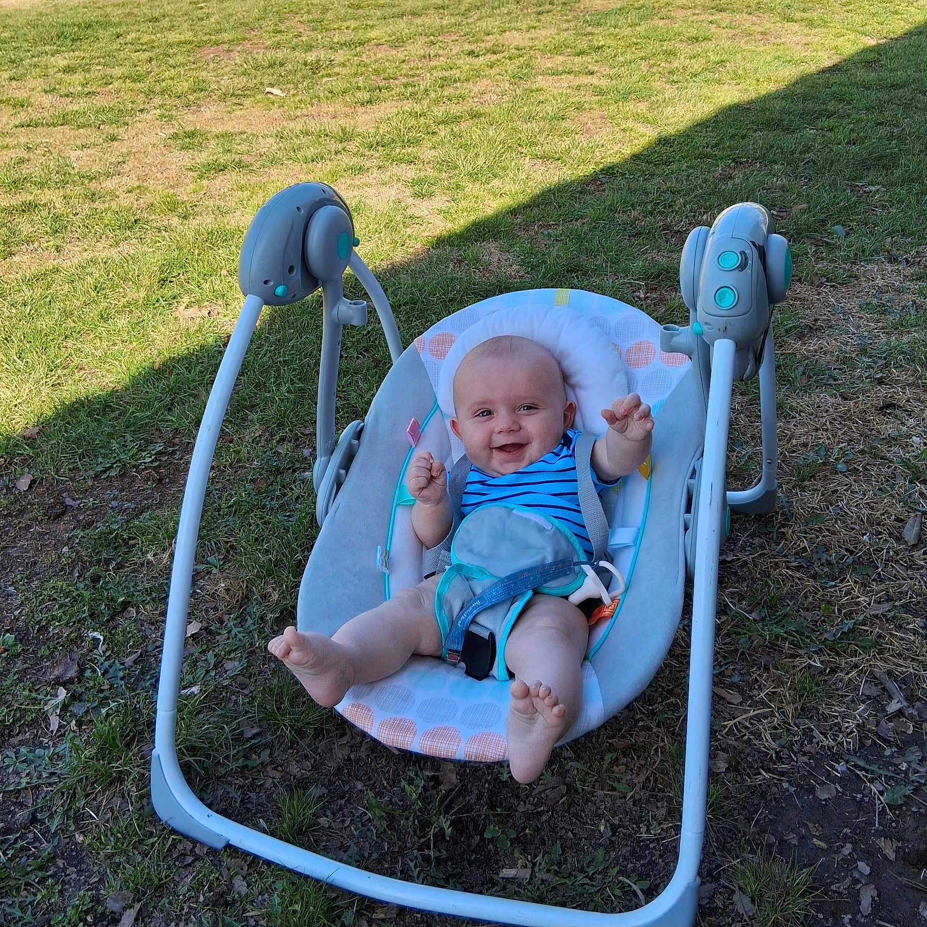 Brandon is registered to the contest to win money with this photo: baby, baby_swing, outdoor, grass, smiling, happy, infant, child, blue_clothing, play, sunlight, nature, seat, toy, grass_field, summer, cute, person, barefoot, relaxing