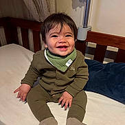 Dario participe au concours pour gagner de l'argent avec cette photo : baby, infant, smiling_child, joyful_expression, pajamas, bandana_bib, socks, hands, face, dark_hair, dimples, crib, bed, pillow, wooden_rail, blanket, nursery, portrait, happy, sitting