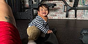 Dario participe au concours pour gagner de l'argent avec cette photo : child, toddler, baby, smiling, indoor, gym, gym_equipment, dumbbell, barbell, exercise_mat, brick_wall, bench, striped_shirt, socks, rubber_floor, crawling, person, tattoo, happy, hair