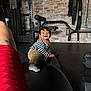 child, toddler, baby, smiling, indoor, gym, gym_equipment, dumbbell, barbell, exercise_mat, brick_wall, bench, striped_shirt, socks, rubber_floor, crawling, person, tattoo, happy, hair