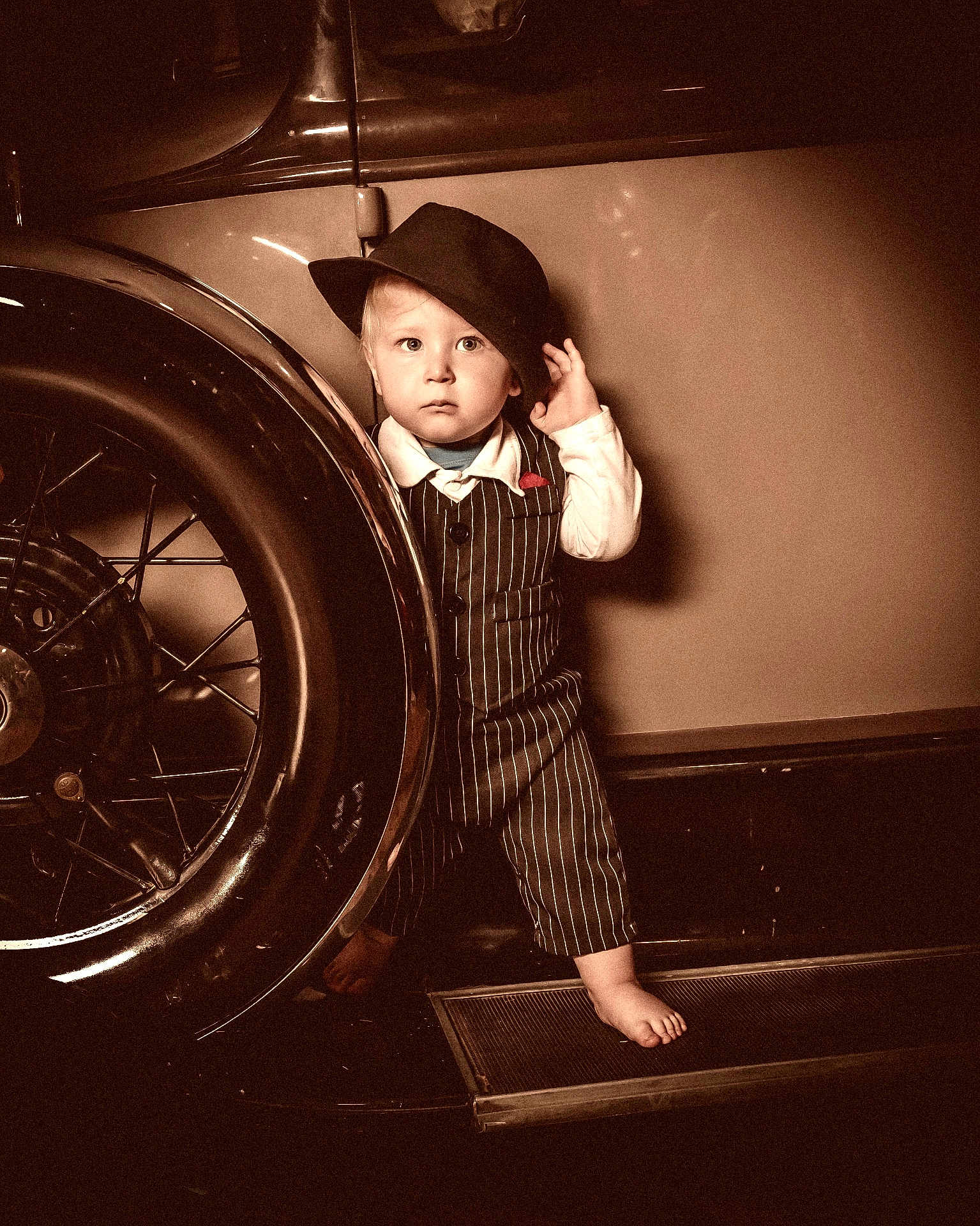 Camden is registered to the contest to win money with this photo: toddler, child, vintage_car, hat, pinstripe_suit, barefoot, wheel, oldtimer, sepia, portrait, curious, standing, retro, classic, vehicle, person, clothing, sidewalk, expression, nostalgic