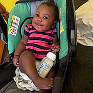 Kylie joined the competition — help win amazing prizes! baby, infant, bottle, smiling, baby_carrier, striped_clothing, blanket, foot, hand, face, indoor, cushion, child, person, furniture, seat, happy, cute, skin, portrait