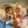 child, baby, siblings, bed, pillow, floral_pattern, onesie, tshirt, shorts, smiling, laying_down, indoor, cute, family, infant, happy, person, home, lightning_mcqueen, candid