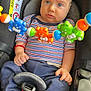 Yannis a rejoint le concours — aidez-le/la à gagner de superbes lots ! baby, car_seat, toy, striped_shirt, blue_pants, socks, face, hand, seatbelt, child, infant, plastic_toy, colorful, blue, orange, green, indoor, sitting, serious_expression, safety