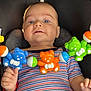 Yannis a rejoint le concours — aidez-le/la à gagner de superbes lots ! baby, child, car_seat, toy, plastic_toy, teddy_bear, striped_shirt, blue_eyes, hand, infant, colorful, closeup, indoor, playtime, cute, smiling, person, seat, clothing, baby_toy