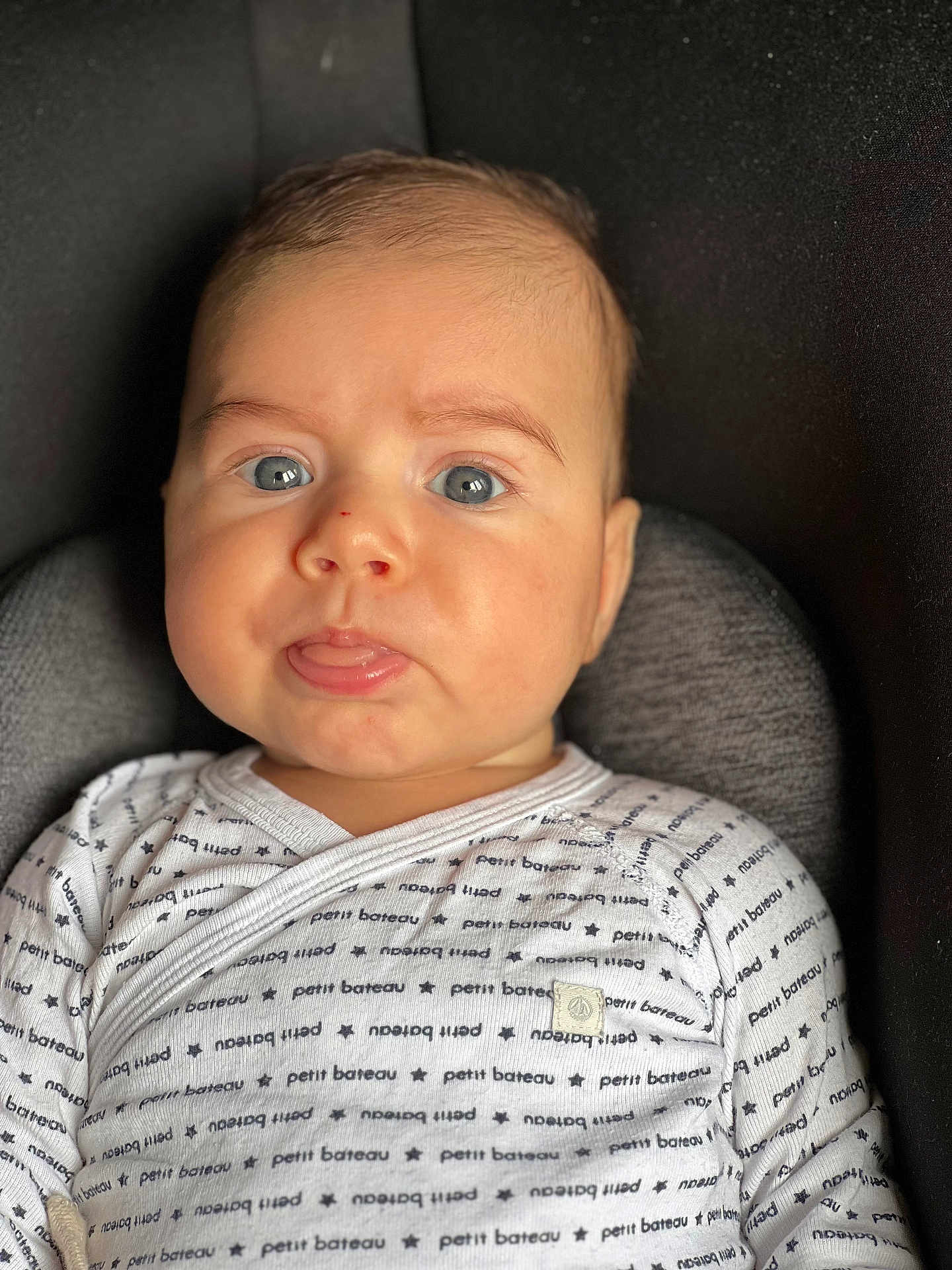Yannis participe au concours pour gagner de l'argent avec cette photo : baby, infant, child, face, blue_eyes, tongue, onesie, clothing, patterned_clothing, seat, cushion, portrait, close_up, indoor, cute, expression, skin, head, person, newborn