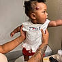 toddler, child, person, tattoo, hair_puffs, white_top, red_shorts, bathroom, sink, hairbrush, curious, standing, holding_hands, toilet, wall, countertop, shoe, footwear, skin, indoor